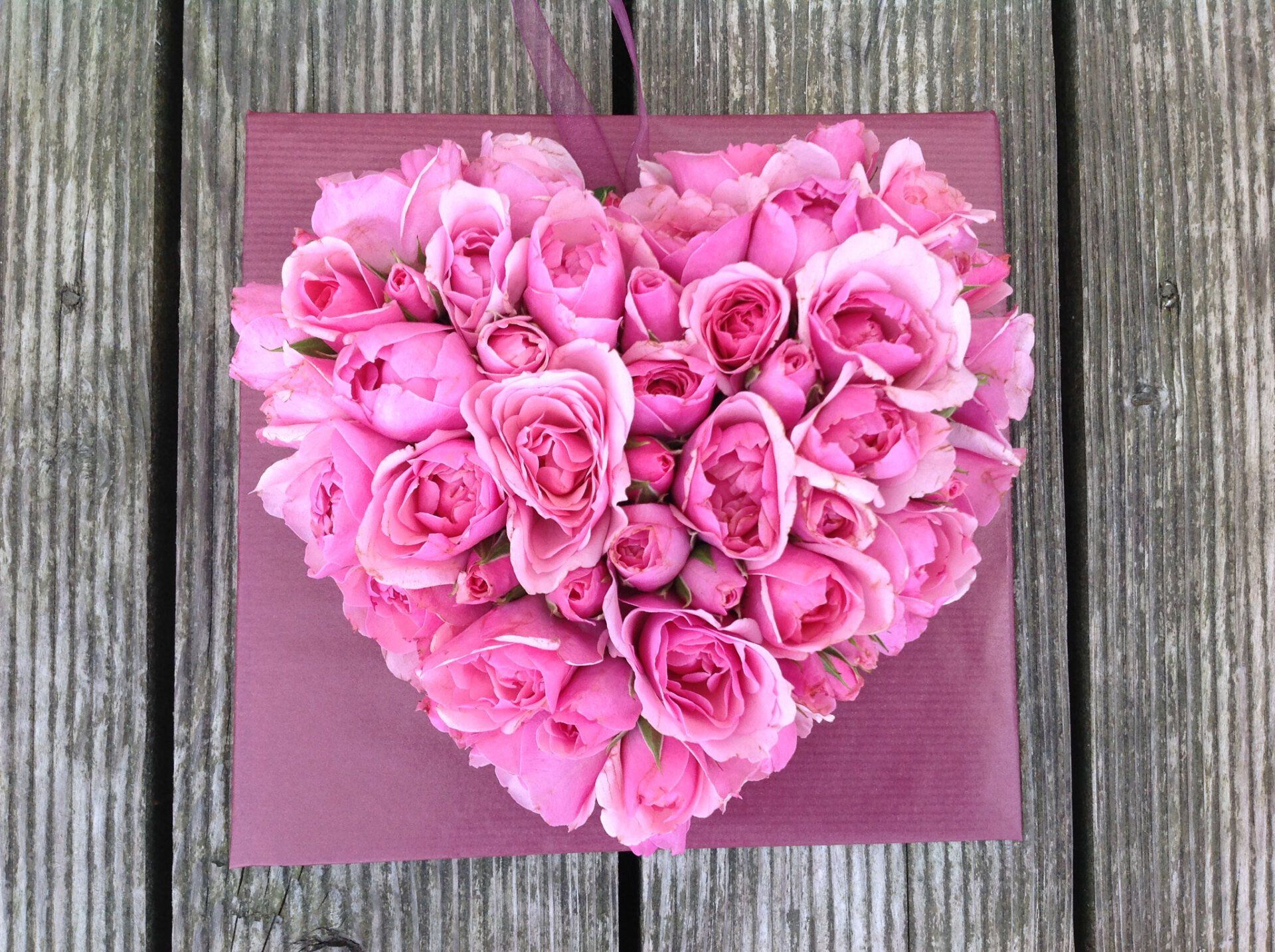 Auf einem Holztisch liegt ein Herz aus rosa Rosen.