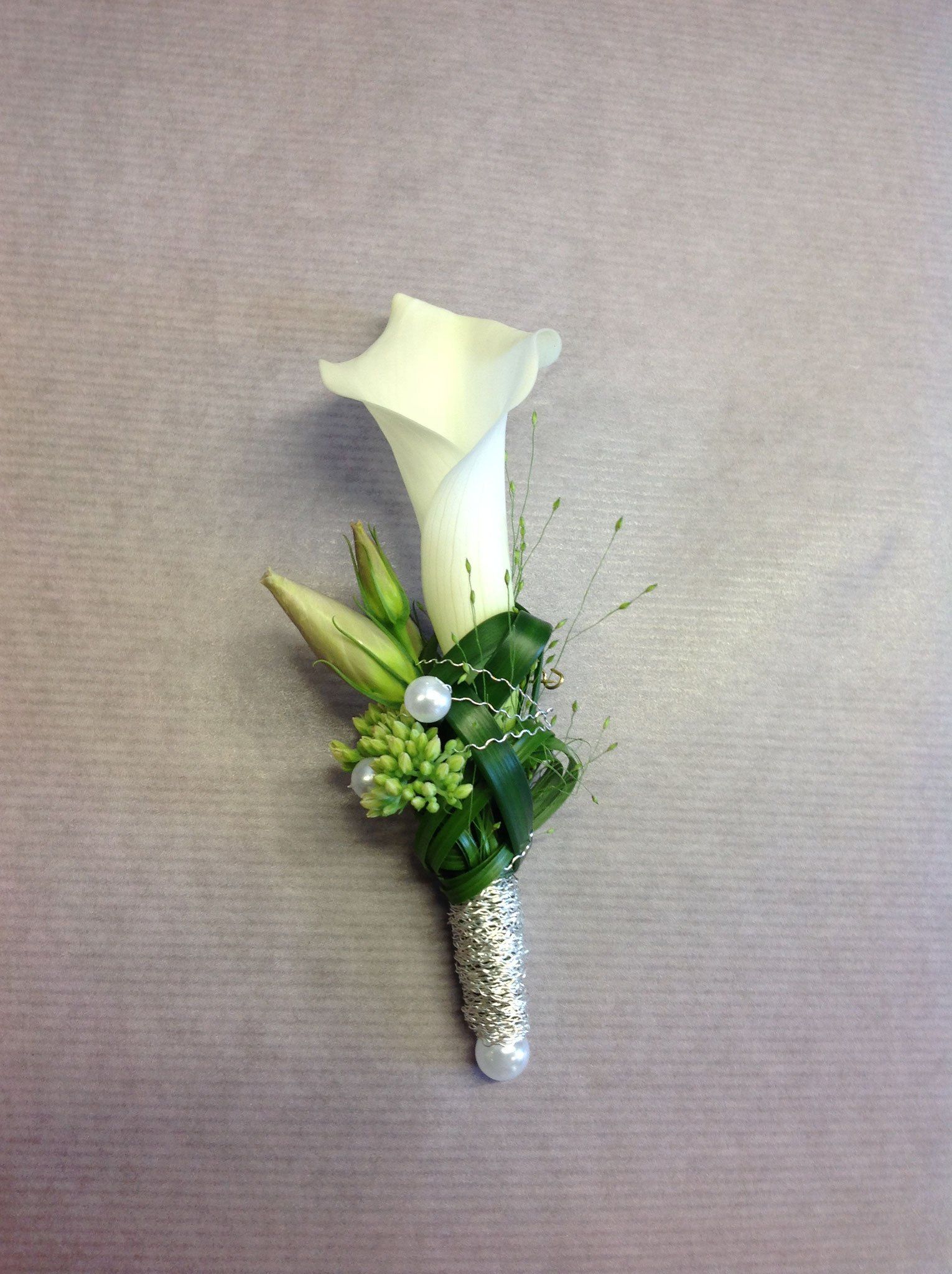 Auf einem Tisch steht eine weiße Blume mit grünen Blättern und Perlen.