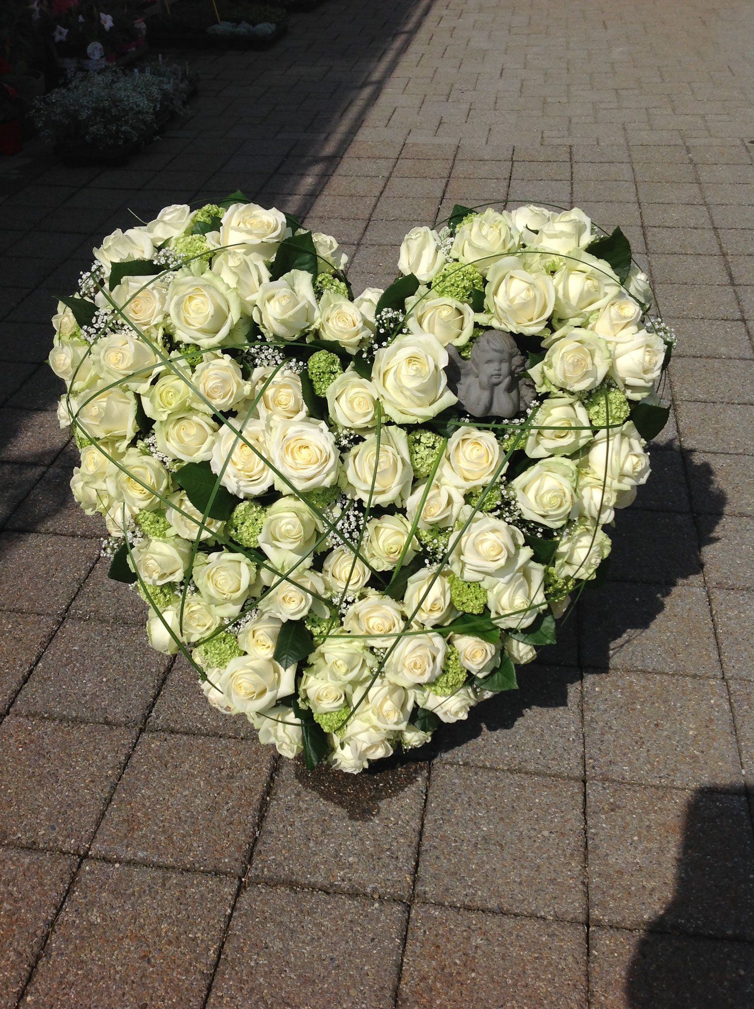 Auf einem gepflasterten Gehweg liegt ein herzförmiger Kranz aus weißen Rosen.