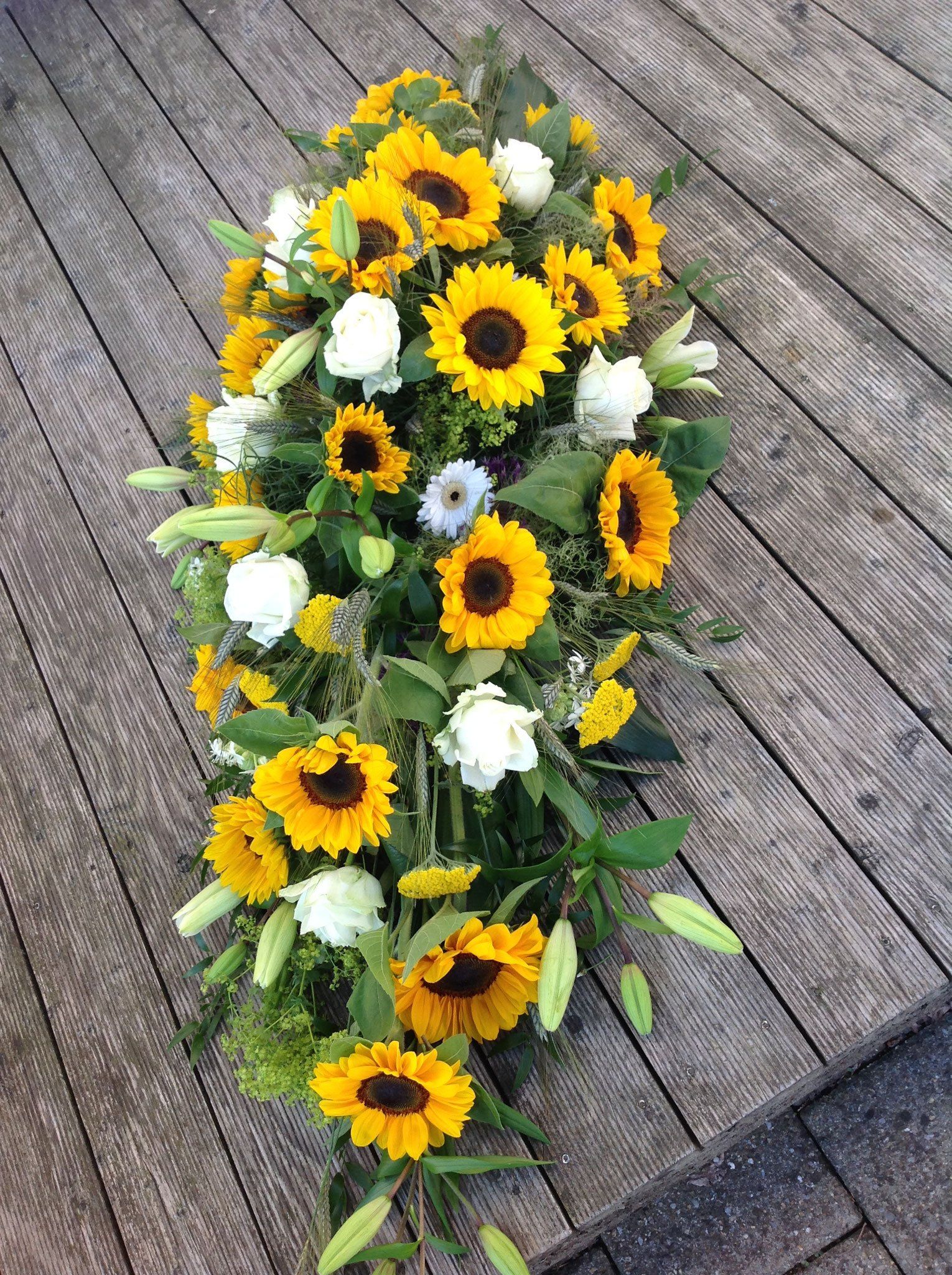 Ein Strauß Sonnenblumen und weißer Blumen steht auf einem Holztisch.
