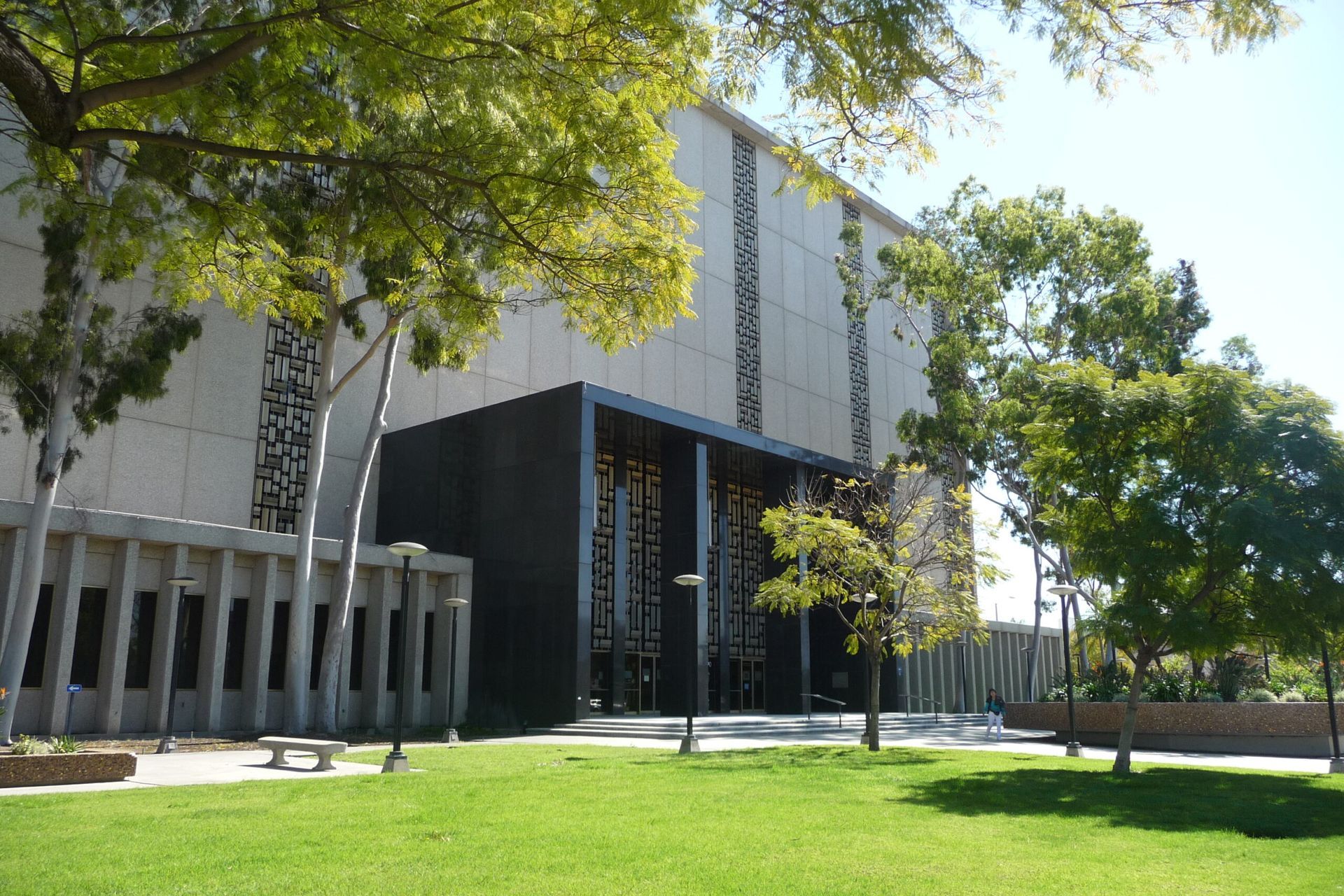 Building exterior with a grassy lawn and trees. Beige and black facade, sunny day.