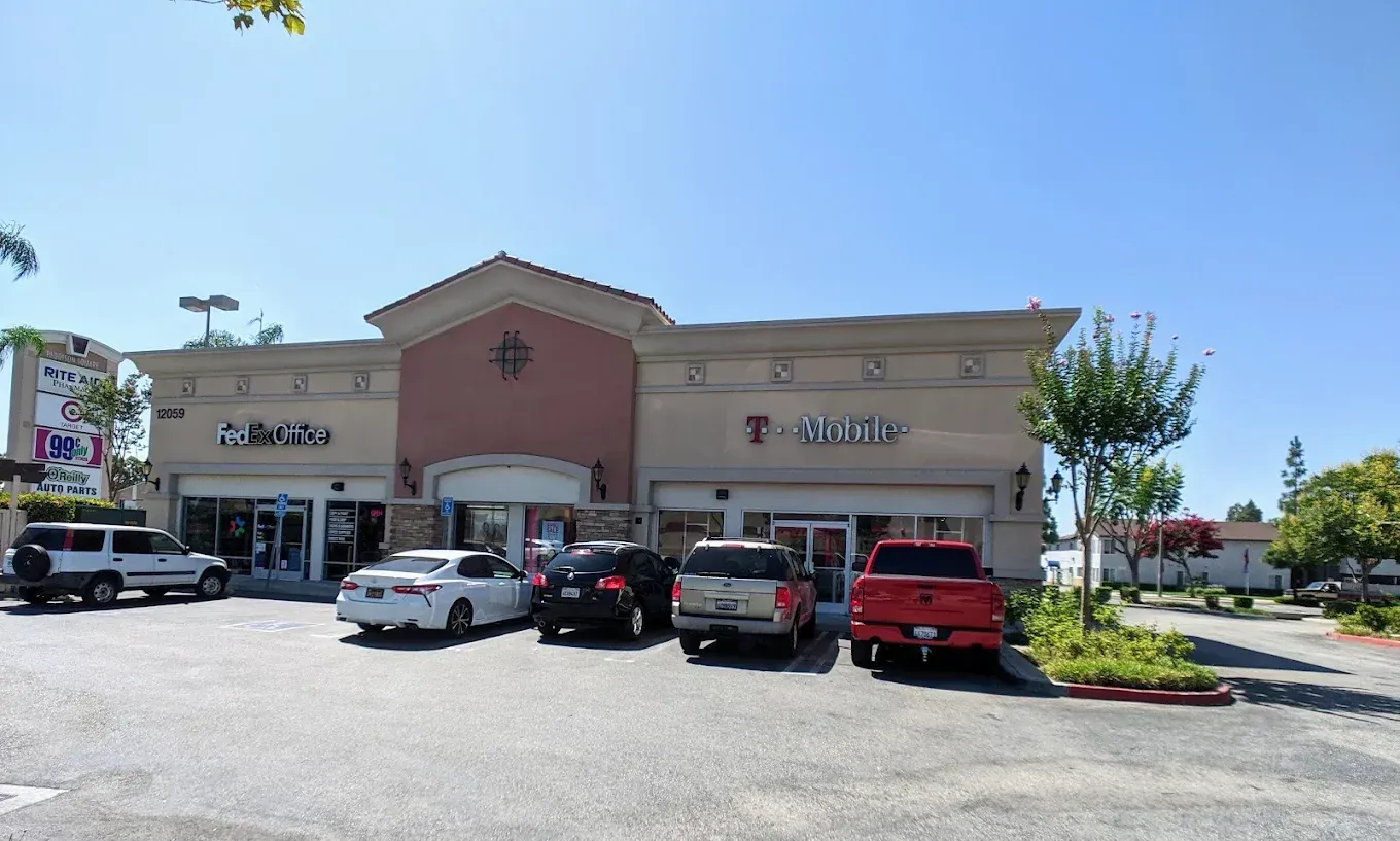 A strip mall with T-Mobile store signs and cars parked out front on a sunny day.