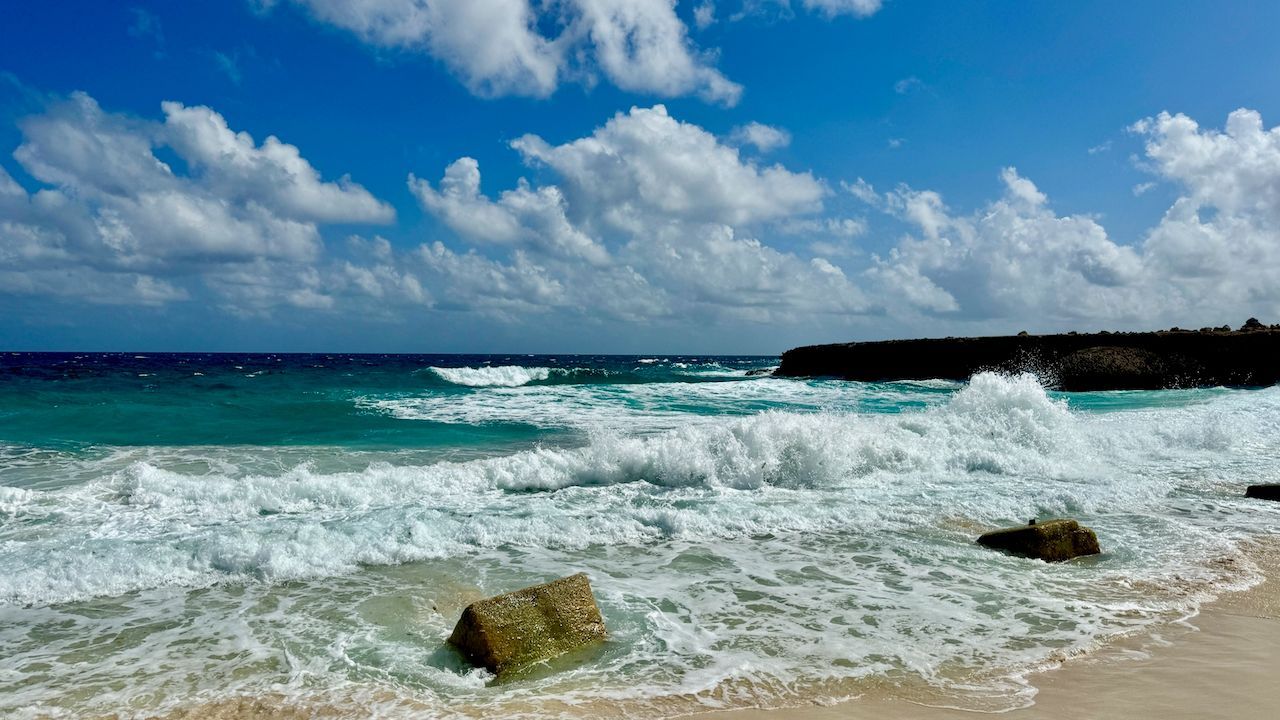 A beach with waves crashing against the rocks on a sunny day.