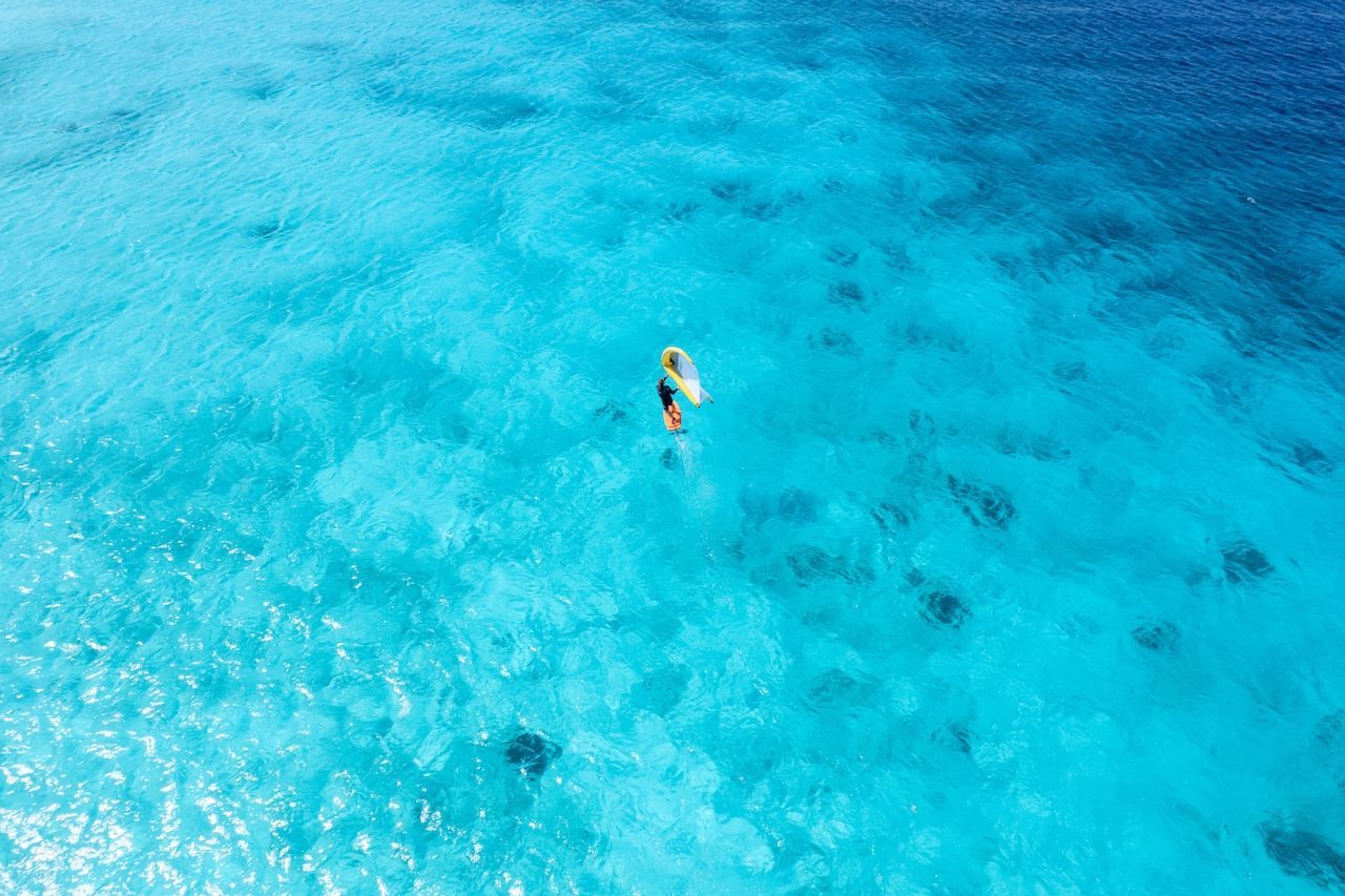 An aerial view of a person holding a surfboard in the ocean. Most beautiful paradise island