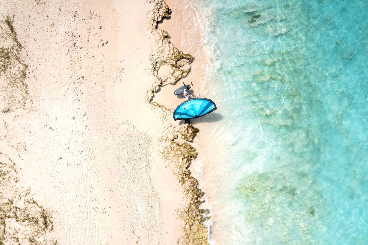 An aerial view of a person standing on a beach holding a surfboard.