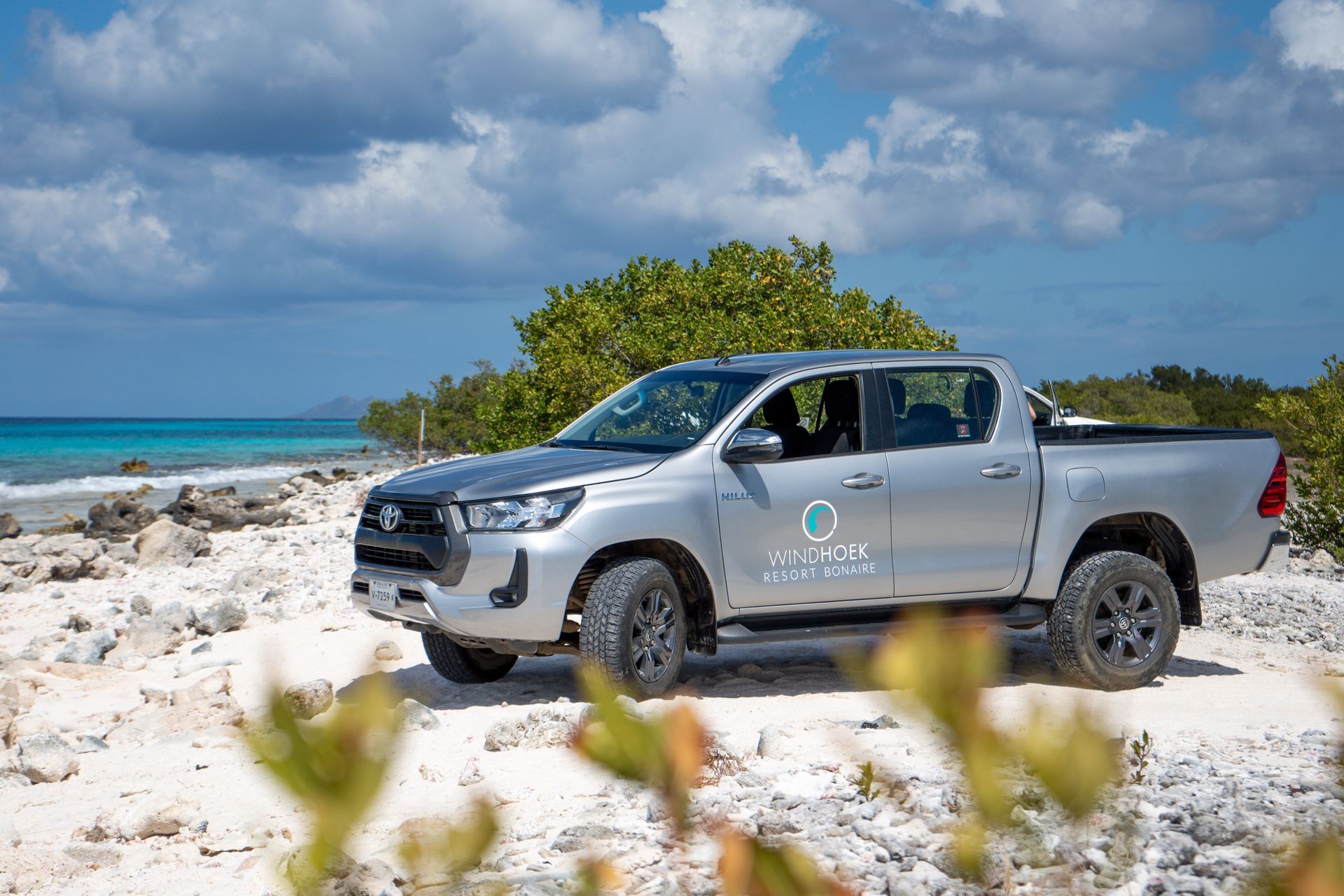 A silver pickup truck is parked on a sandy beach near the ocean.