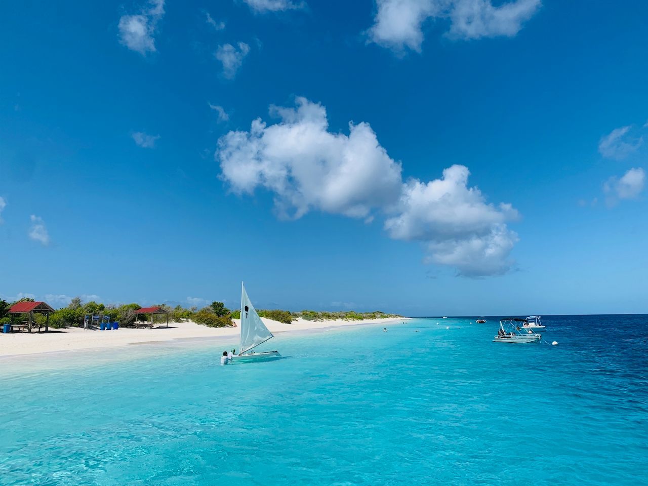 Uitzicht op het turquoise water van Bonaire met een zeilboot en een helderblauwe lucht.