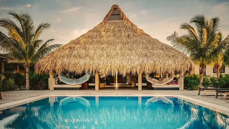 There is a thatched hut overlooking a swimming pool. 