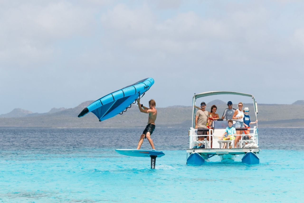 A man is standing on a surfboard in the ocean next to a boat.