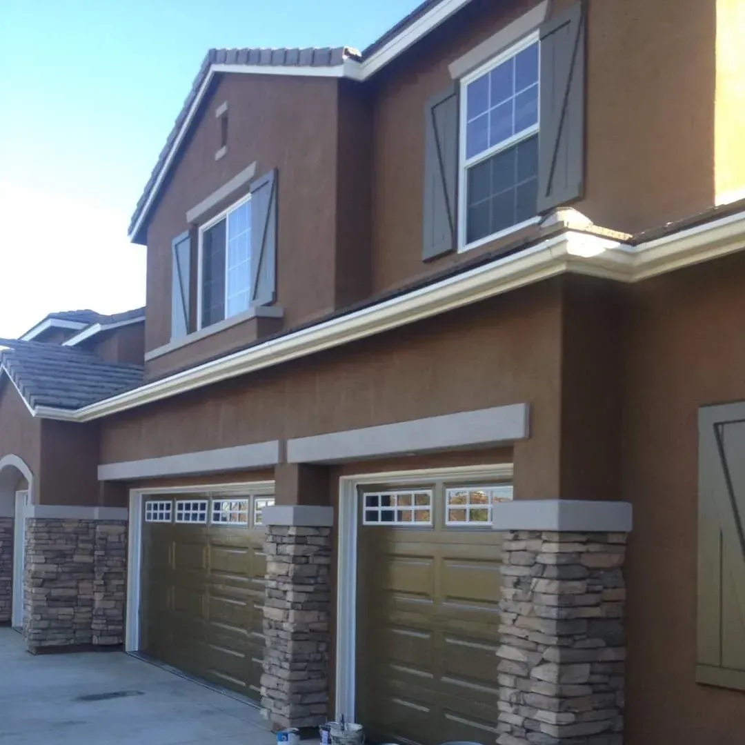 Two-story tan house with stone-accented double garage doors and upper windows