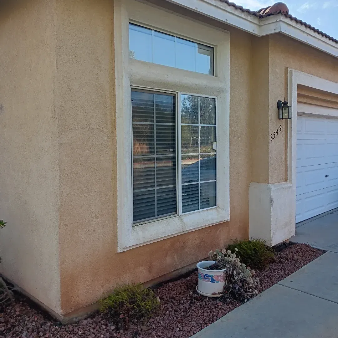 Front exterior of a beige stucco house with a window, garage door, and small desert landscaping.