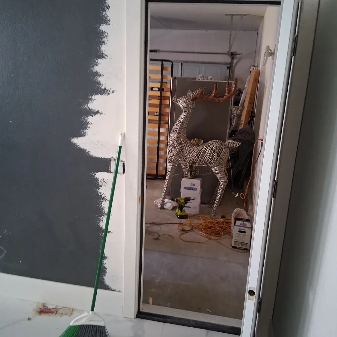 Partially painted room with a foil-covered chair or figure visible through a doorway in a cluttered workshop area