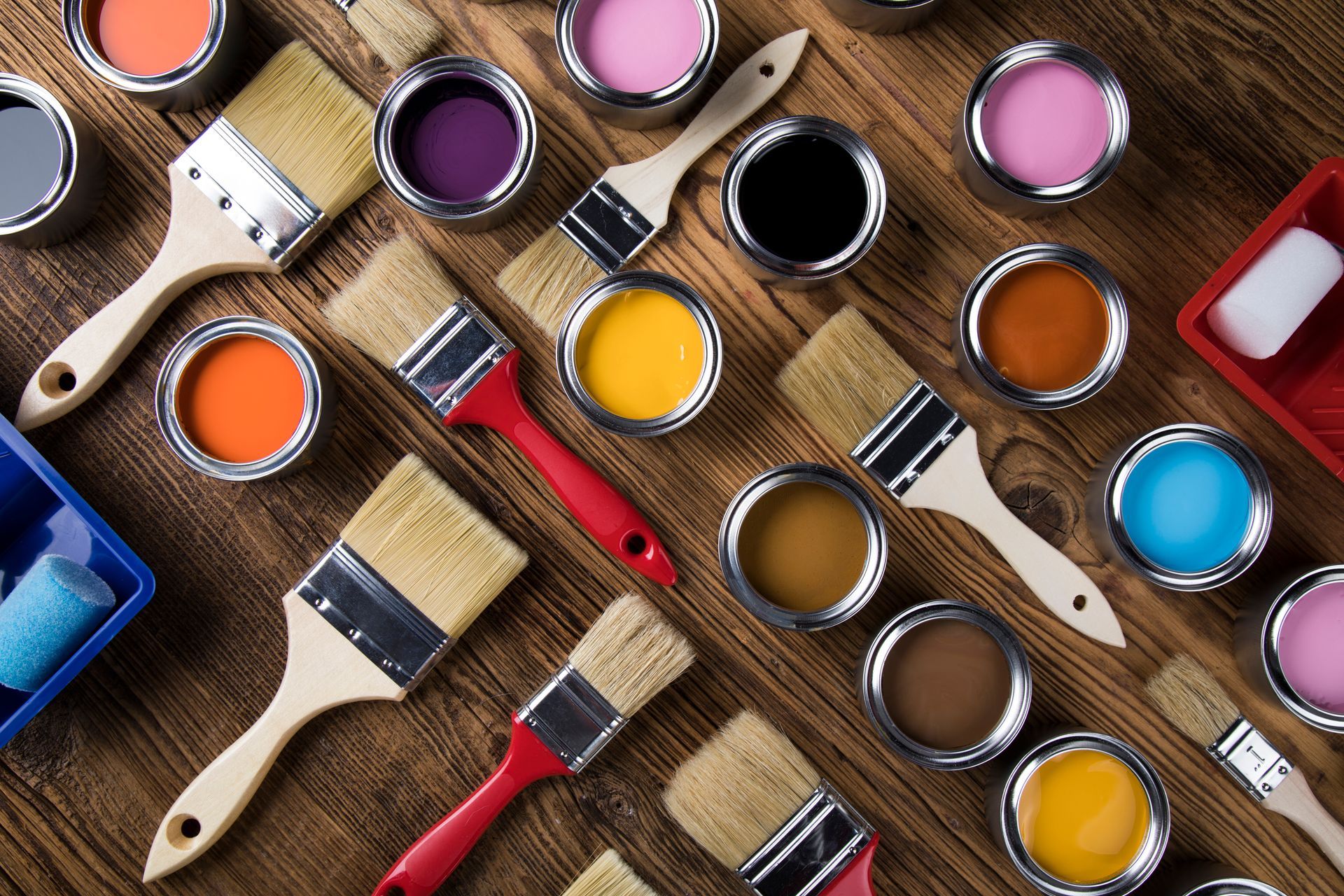 Paint cans and paintbrushes arranged on a wooden surface in assorted bright colors