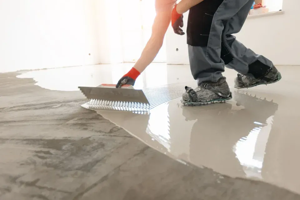Worker spreading gray floor coating with a trowel on a concrete floor