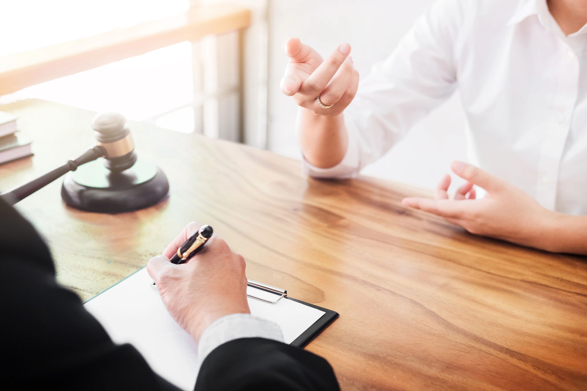 Una persona in giacca e cravatta prende appunti su un blocco per appunti mentre un'altra parla, con un martelletto di legno appoggiato sulla scrivania.