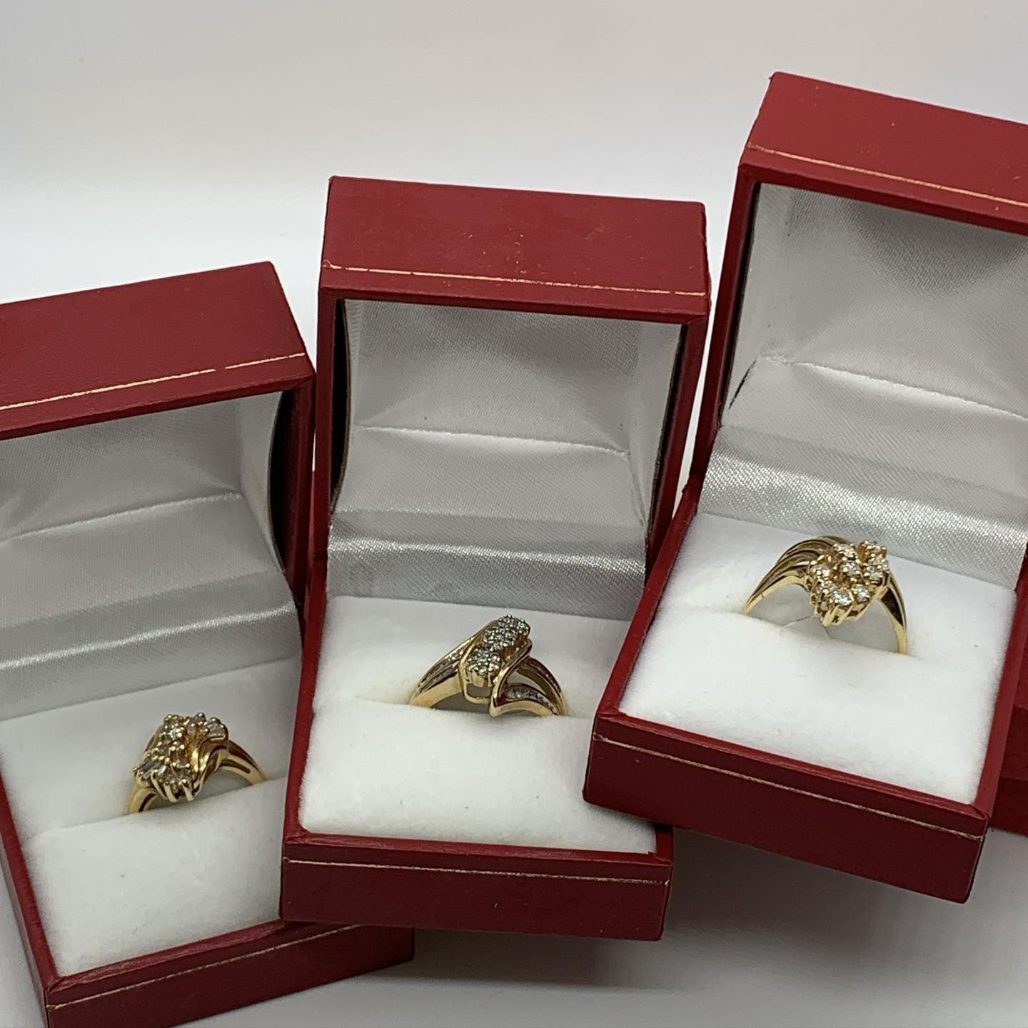 Three gold diamond rings displayed in open red jewelry boxes against a white background.