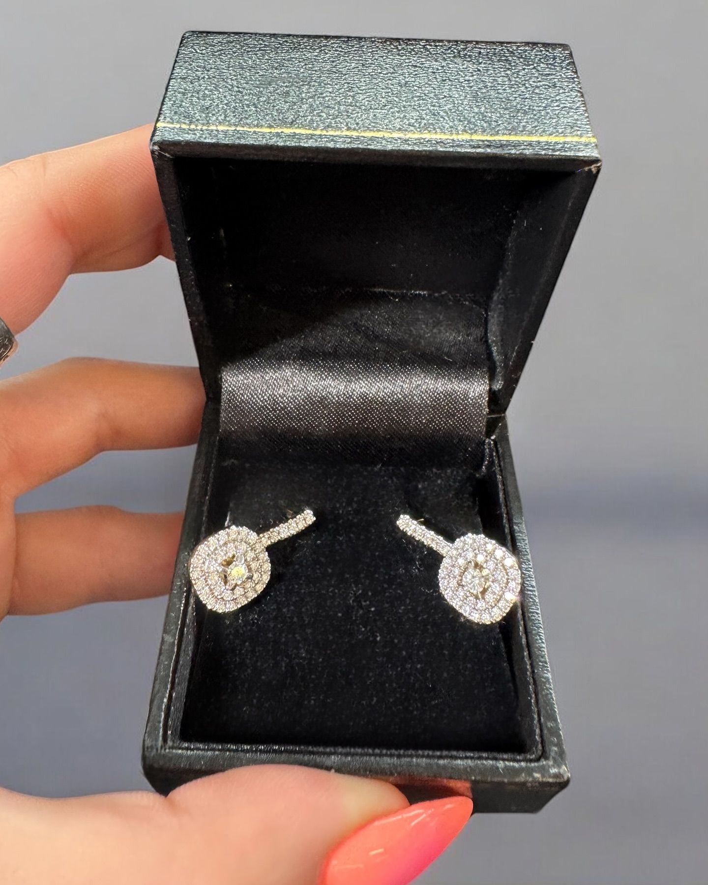 A hand holds a small black jewelry box containing a pair of silver-toned, diamond-studded drop earrings.