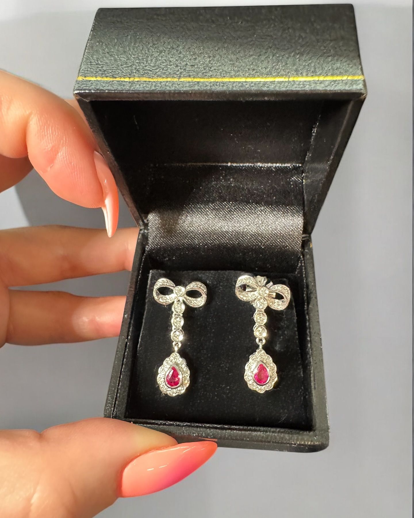 A pair of silver ribbon-shaped earrings with dangling red stones, resting in an open black jewelry box.