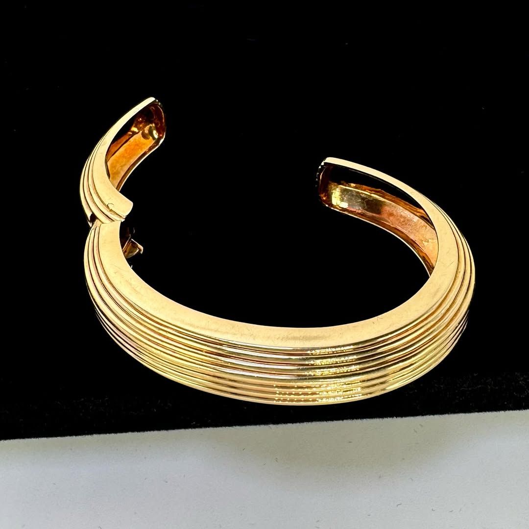 A gold cuff bracelet with horizontal ridged textures, set against a black background.