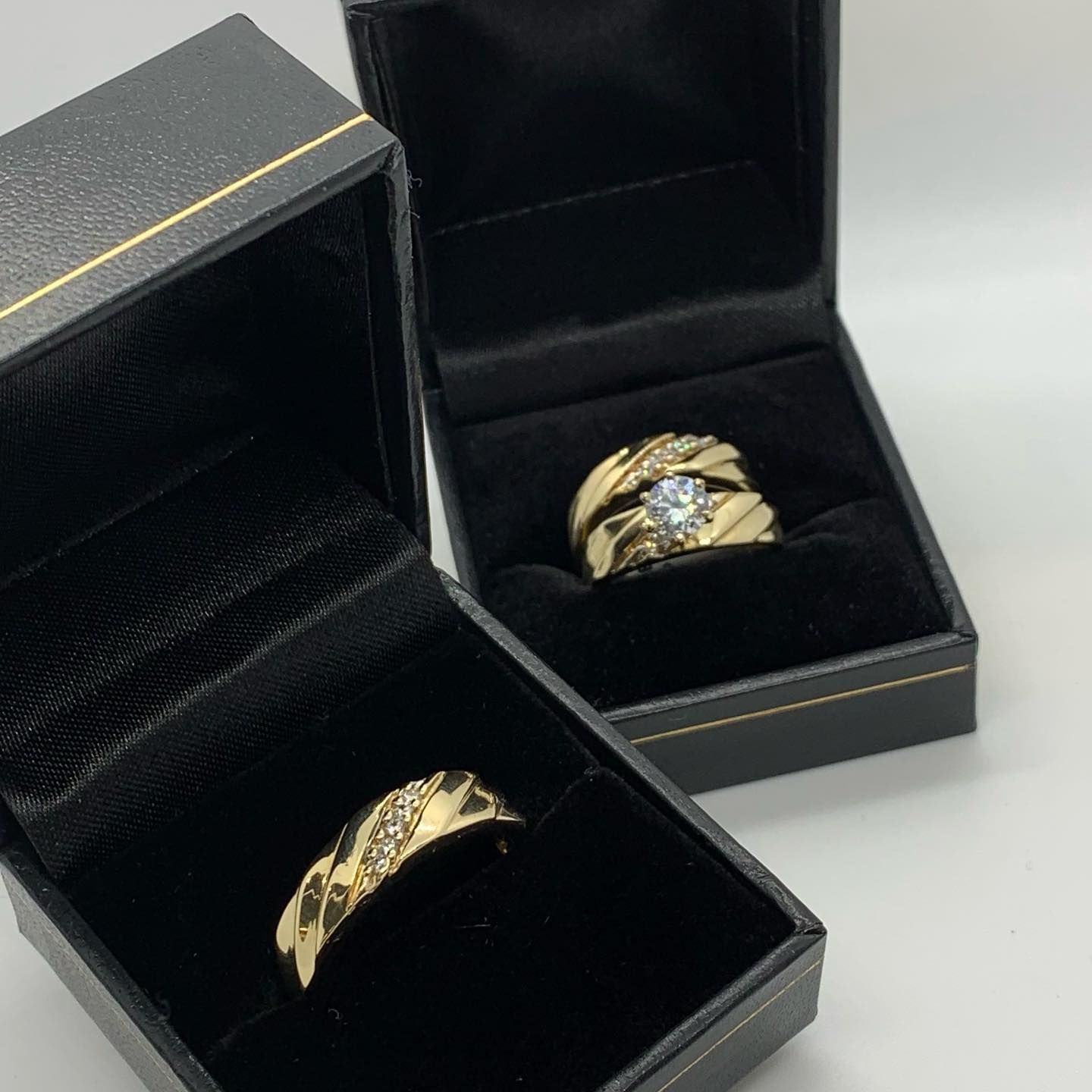 Two gold rings, one with a solitaire diamond and one with a diamond band, displayed in separate black jewelry boxes.