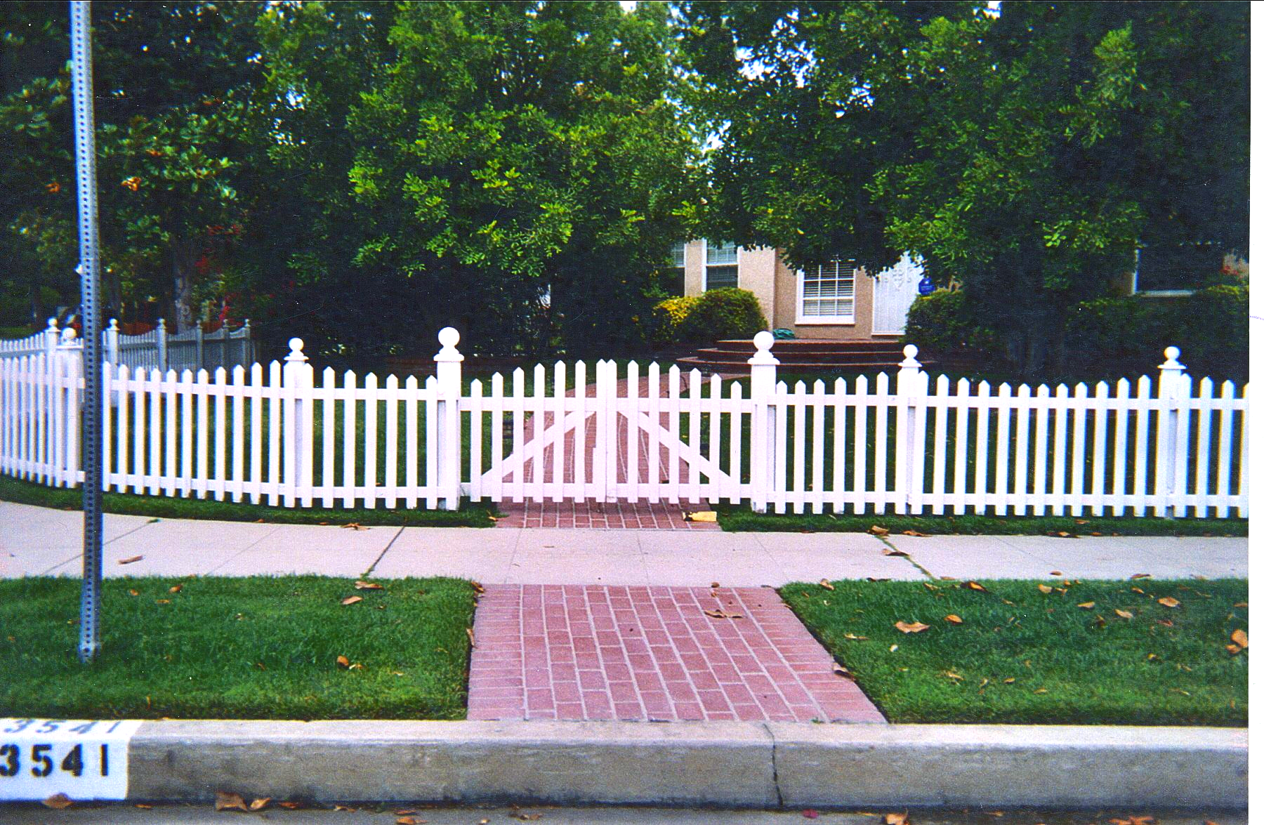 A white picket fence surrounds a house with a brick walkway