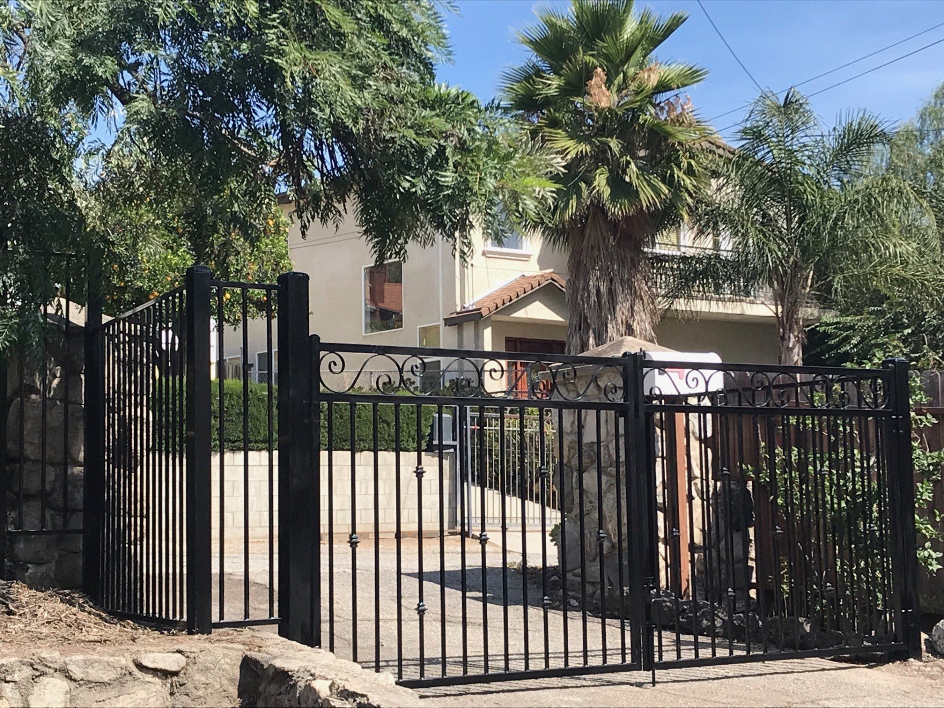 A black fence surrounds a driveway leading to a house
