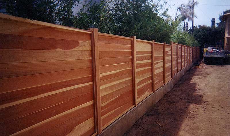 A wooden fence is sitting on the side of a dirt road.