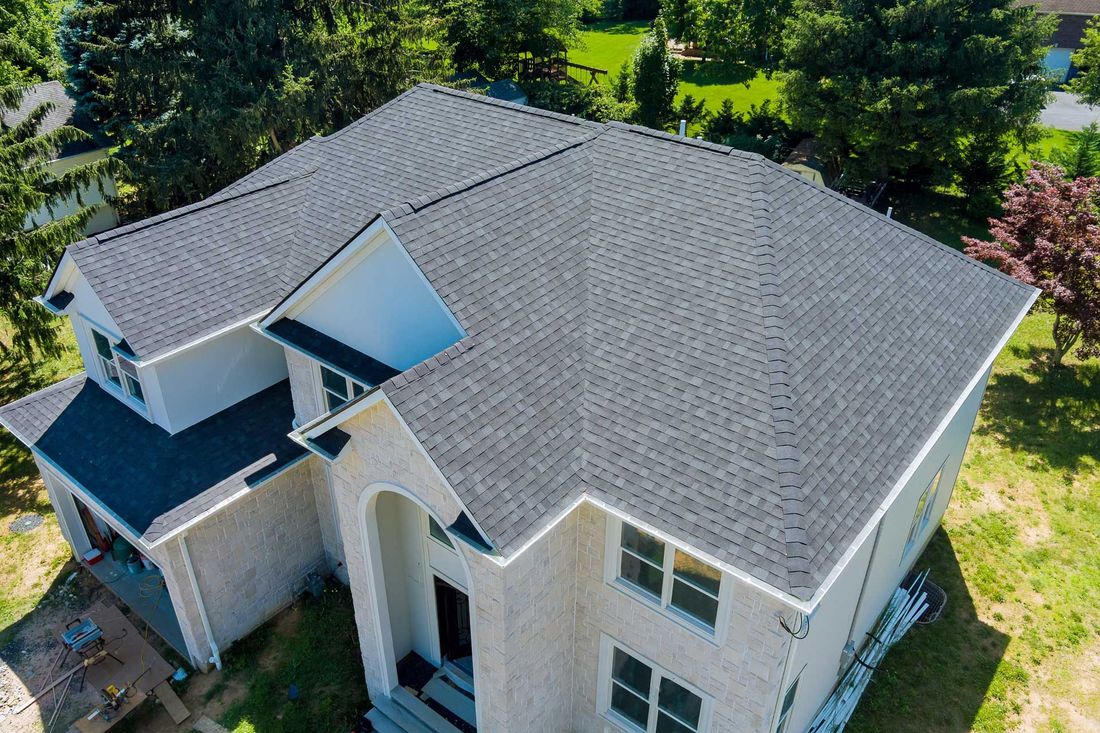 Dark gray shingled roof on a two-story beige house; aerial view.