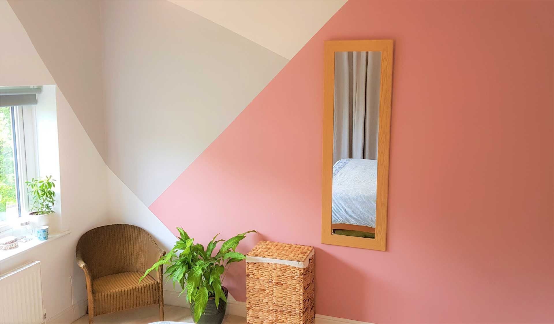 Bedroom with pink, gray, and white geometric wall paint, a mirror, chair, plants, and a woven basket.