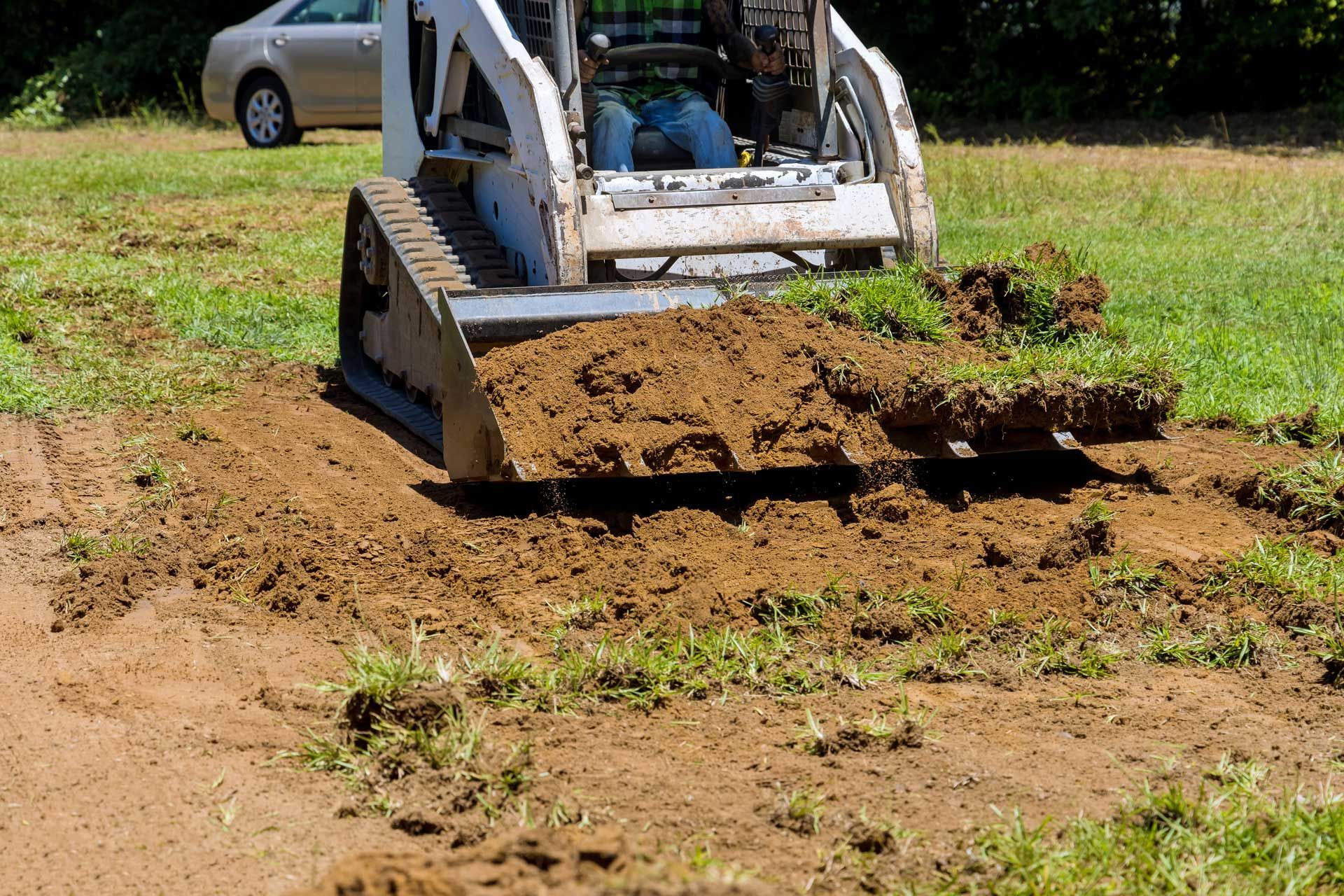 Bobcat removes dirt and grass from a grassy area.