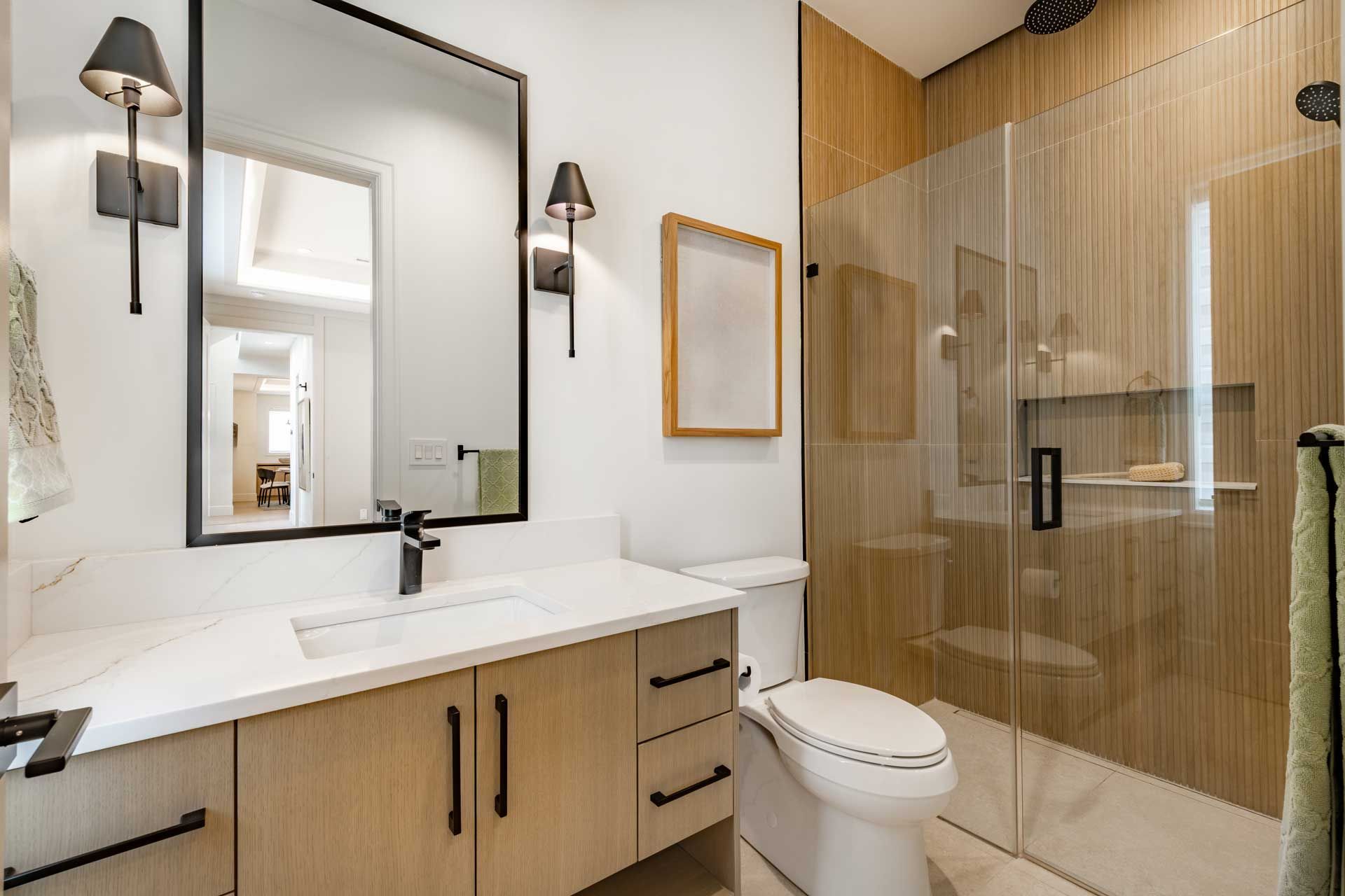 Bathroom with white countertop, wood-tone vanity, large mirror, glass shower, and toilet.