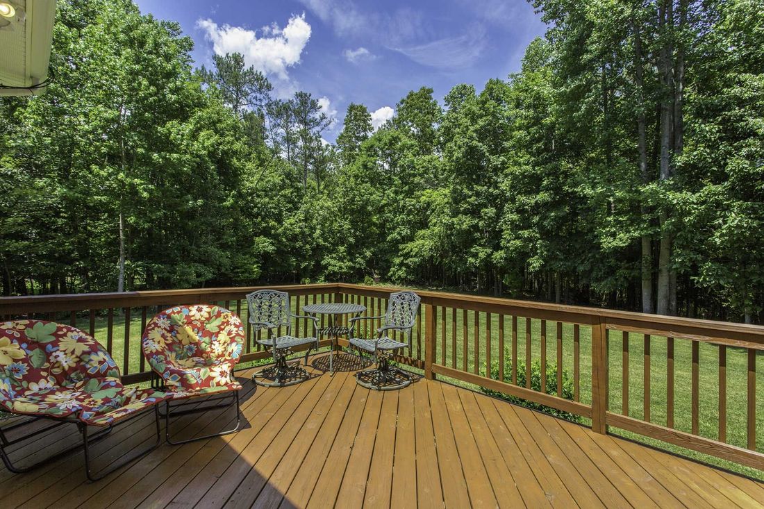 Wooden deck with chairs and table overlooking a green yard and trees under a blue sky.