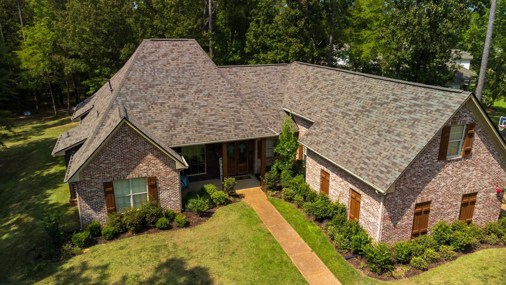 Brick house with brown roof and shutters, front yard, and walkway.