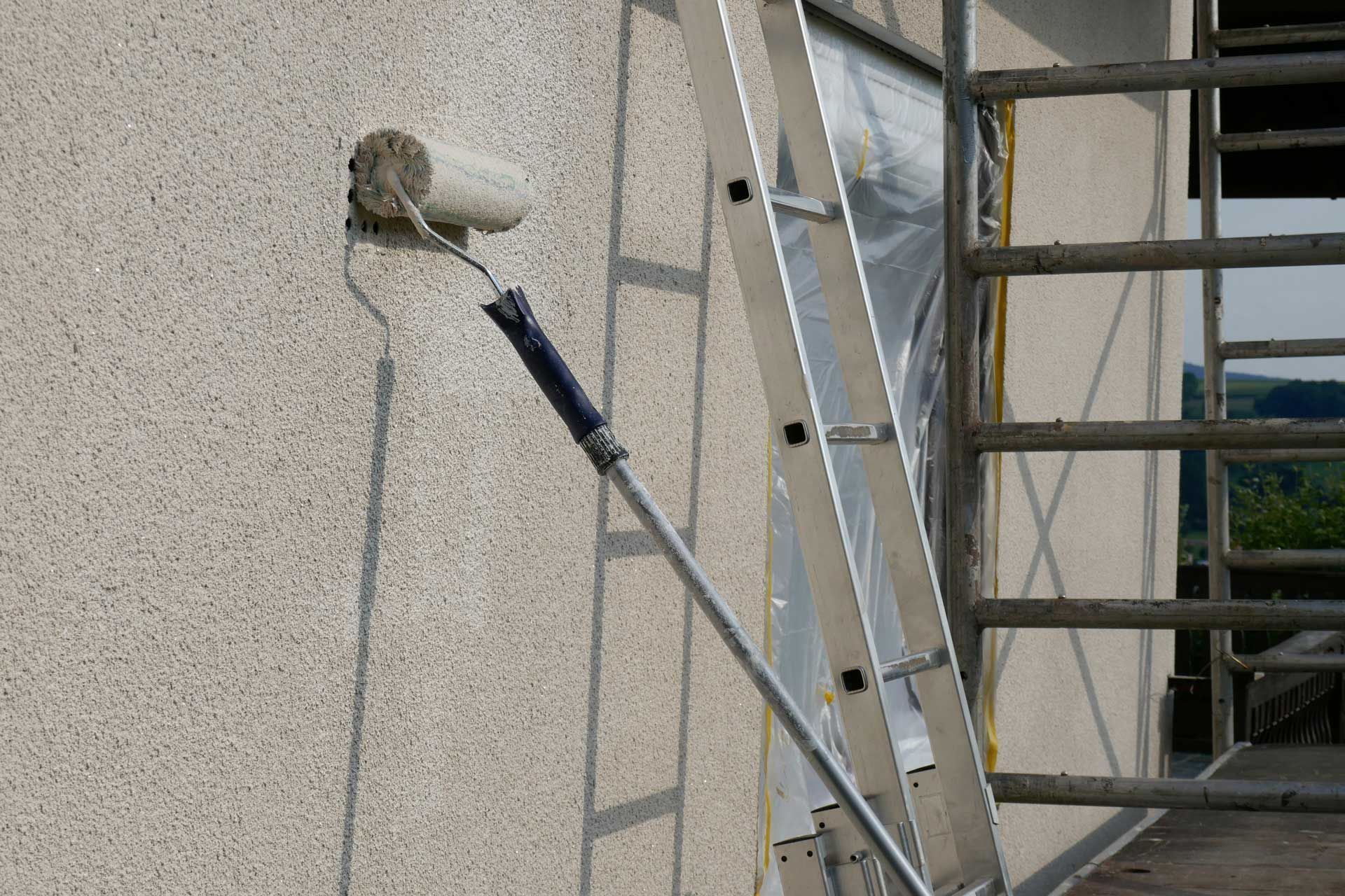 Paint roller applying paint to textured wall next to a ladder and scaffolding.