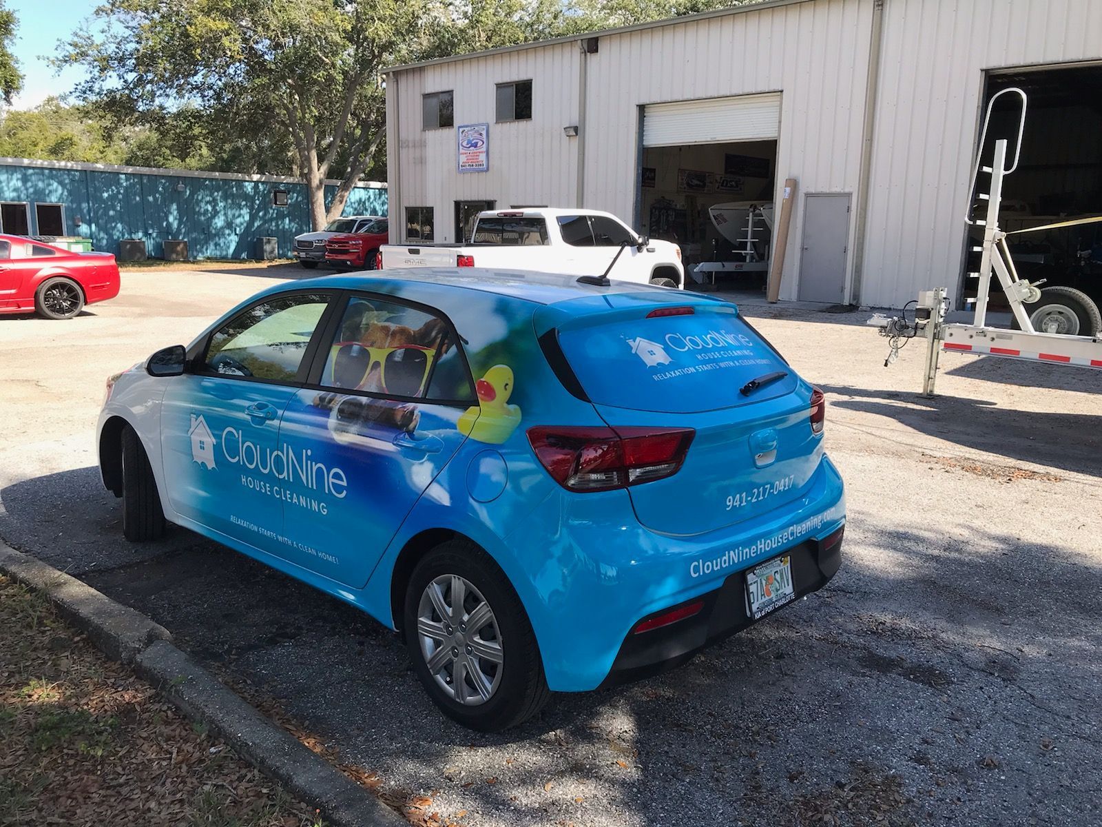 Blue car with Cloud Nine advertising wrap parked in front of a building with open garage doors.