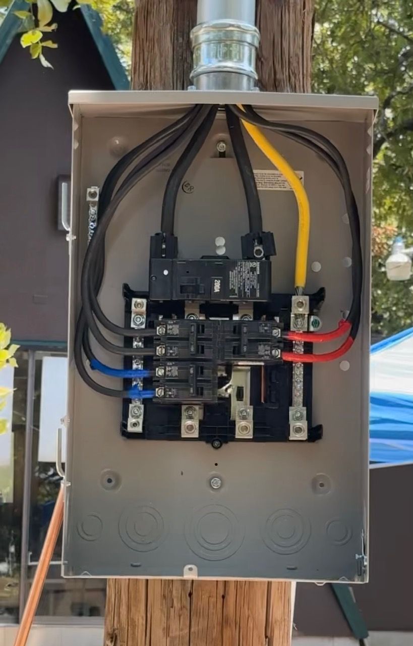 An electrical box is attached to a pole with wires coming out of it