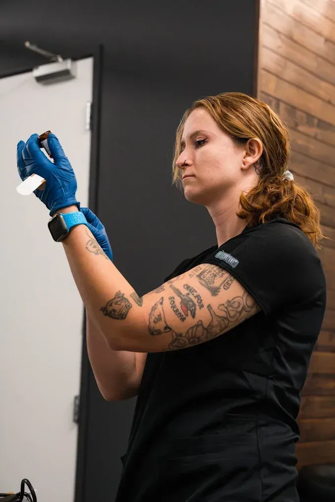 A woman with tattoos on her arm is holding a syringe in her hand.