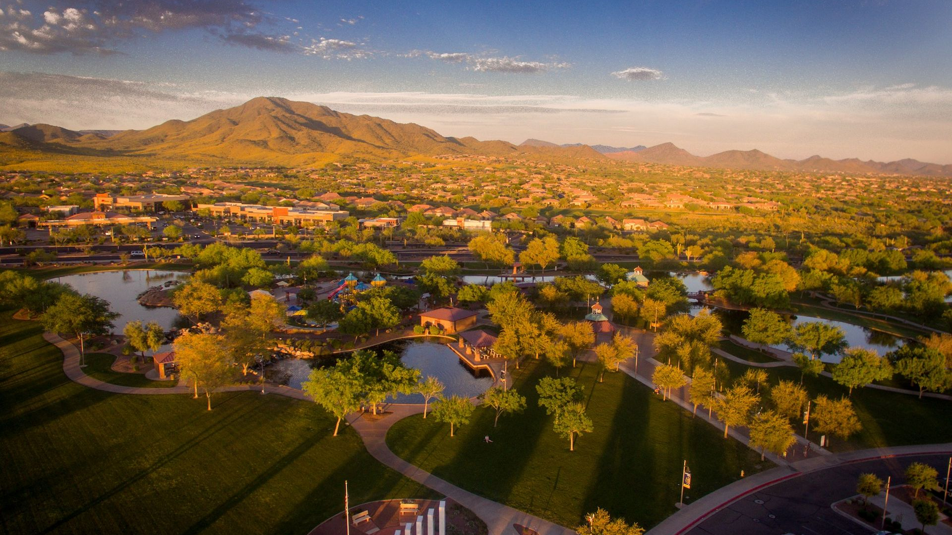 An aerial view of a park with a lake and mountains in the background.