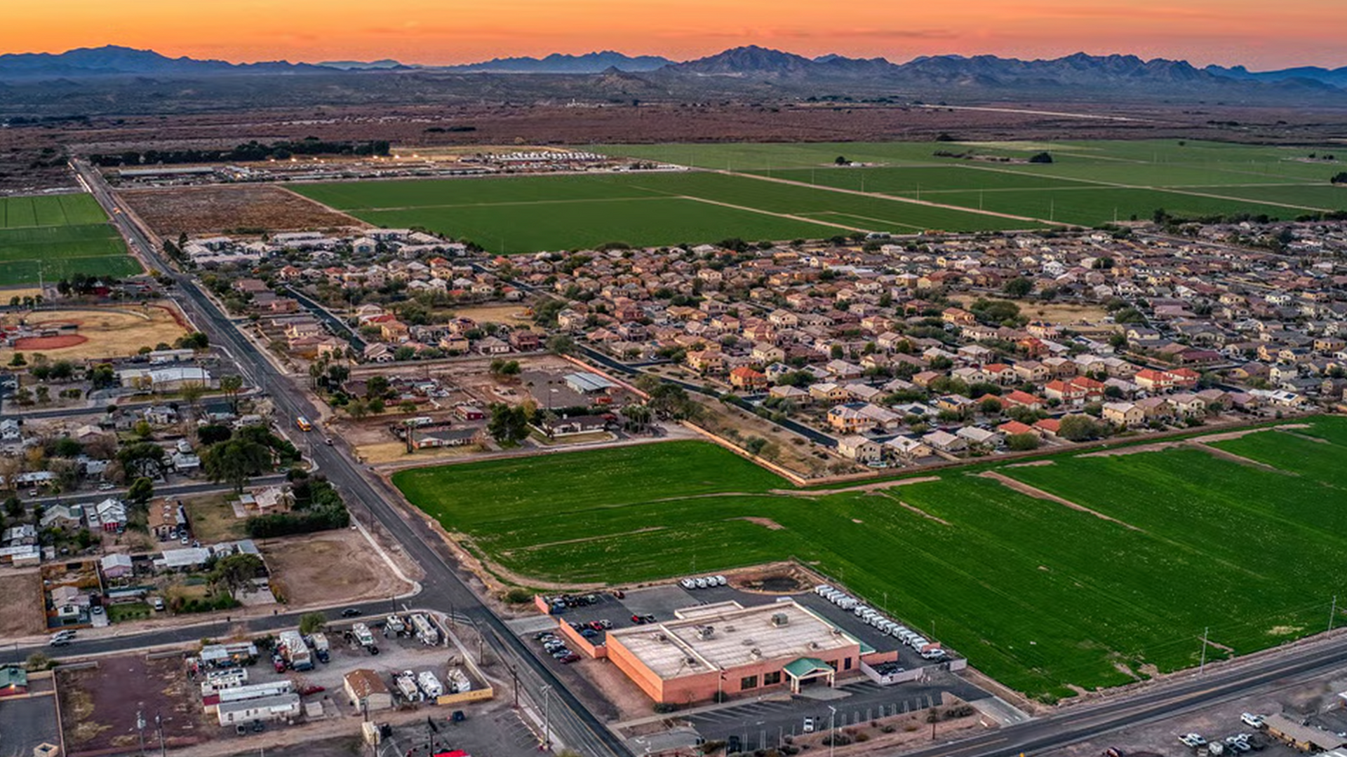 An aerial view of a small town surrounded by fields and mountains at sunset.