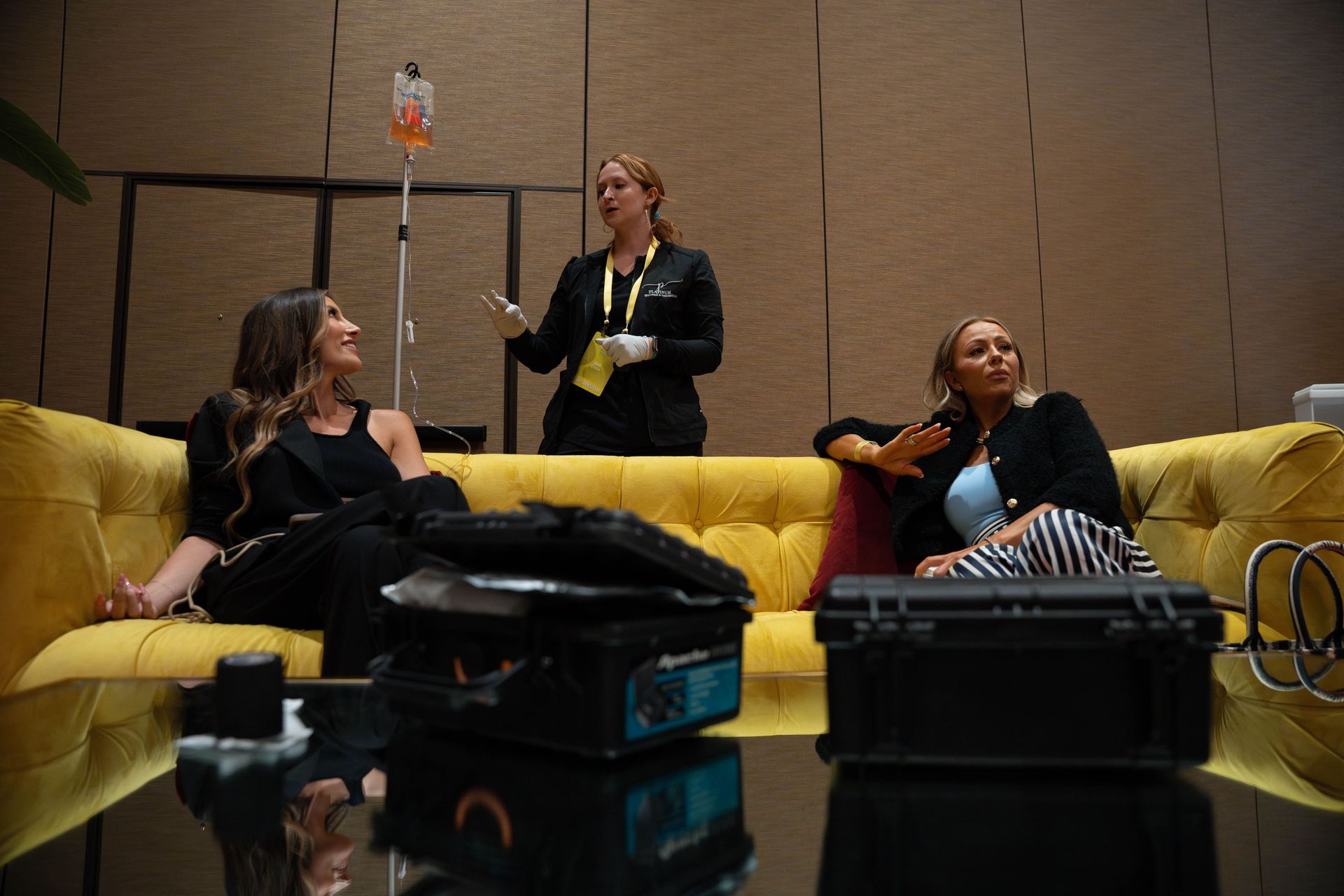 Three women are sitting on a yellow couch talking to each other.