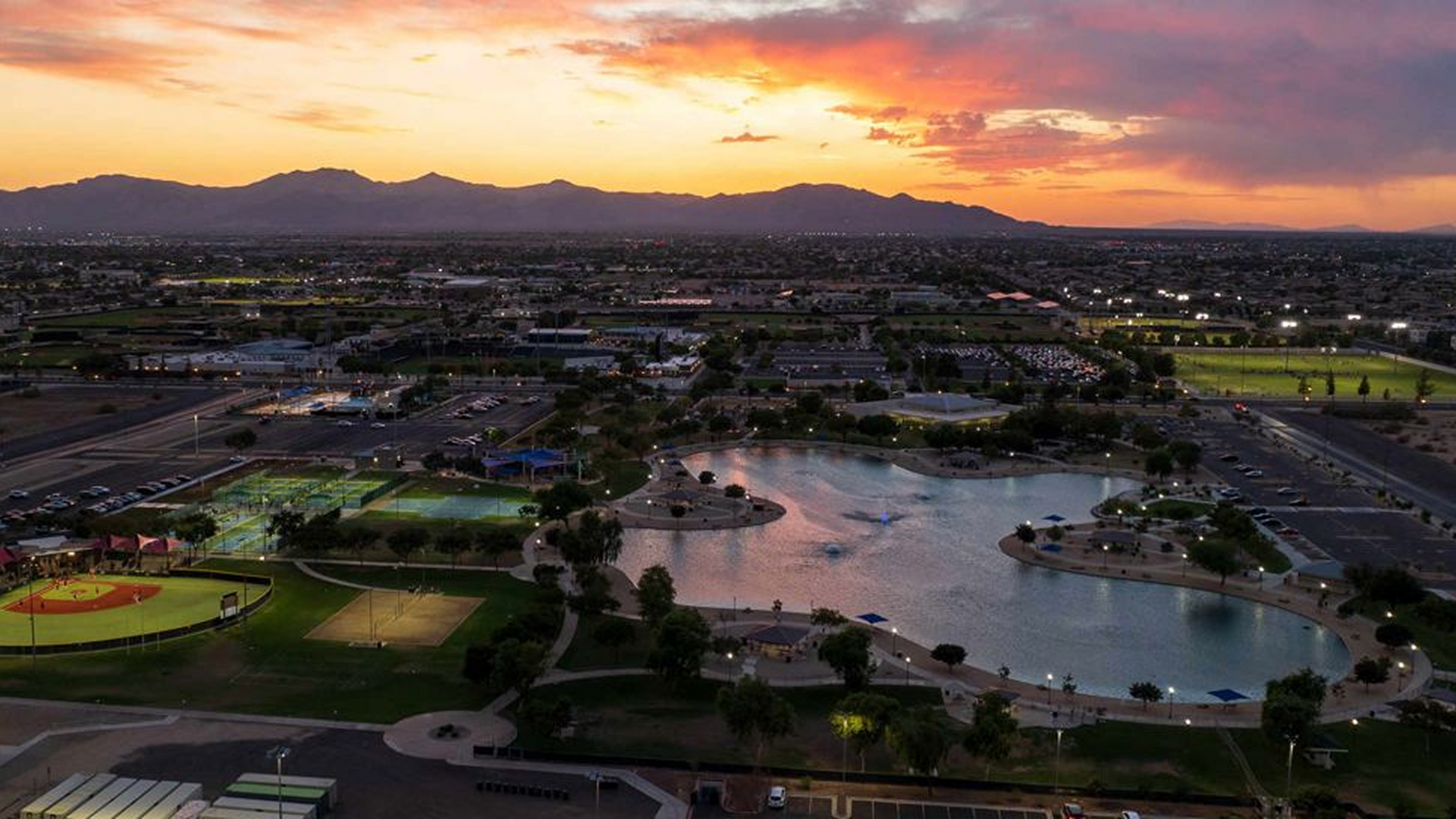 An aerial view of a city with a lake and mountains in the background at sunset.