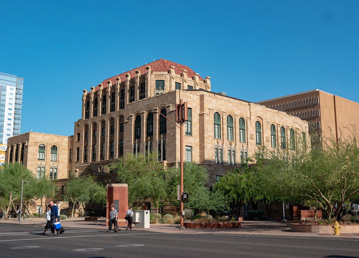 People are crossing the street in front of a large building.