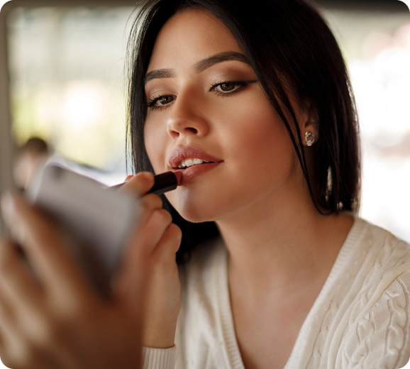A woman is applying lipstick in front of a mirror.