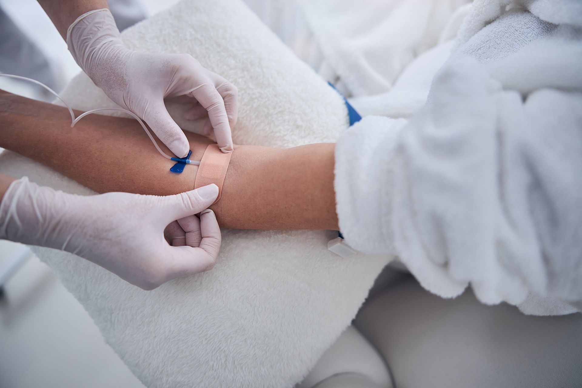 Gloved hands drawing blood from a patient’s arm with a blue syringe in a clinical setting