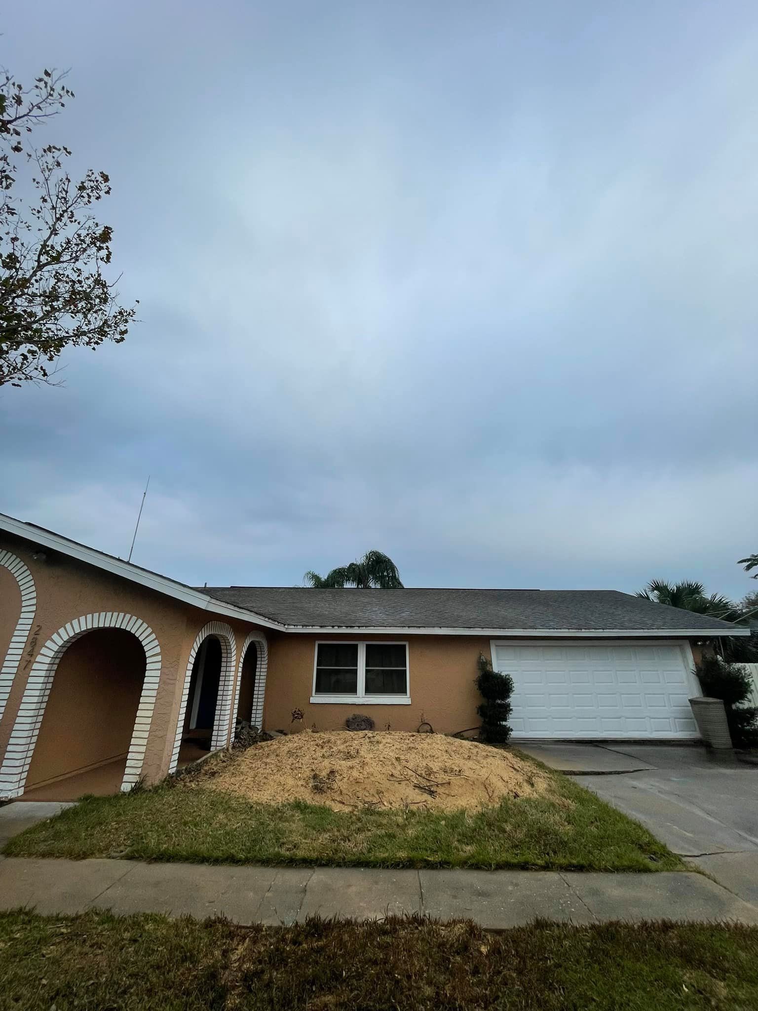 Tan house with sand pile in front, cloudy sky overhead.