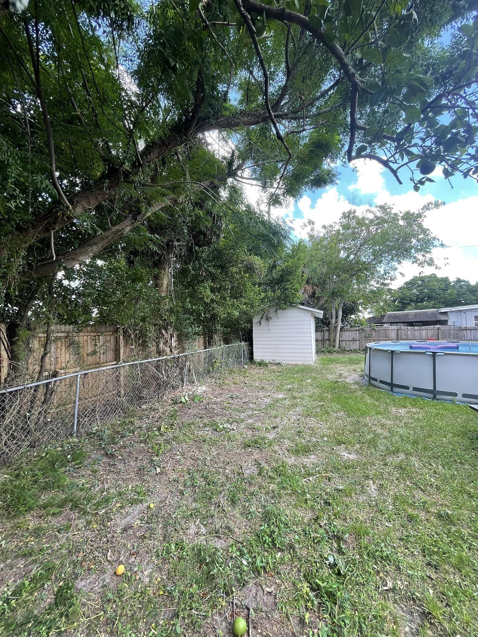 Backyard with trees, shed, fence, and above-ground pool under partly cloudy sky.