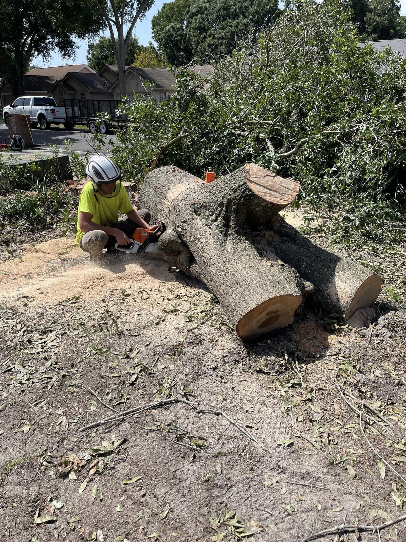 Arborist in yellow shirt cuts a tree trunk with a chainsaw outdoors.