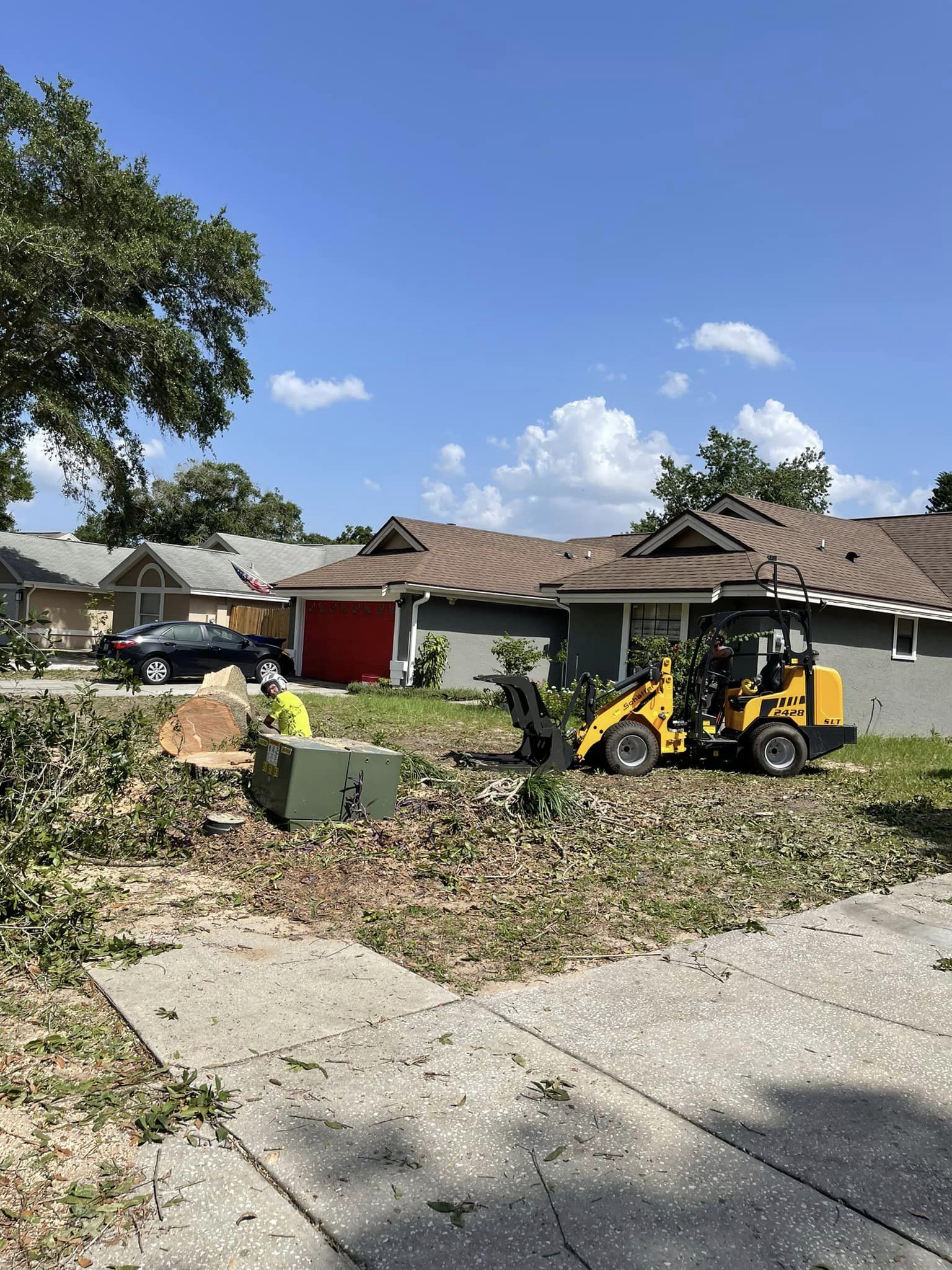 A small yellow construction vehicle working on a yard in a residential neighborhood.