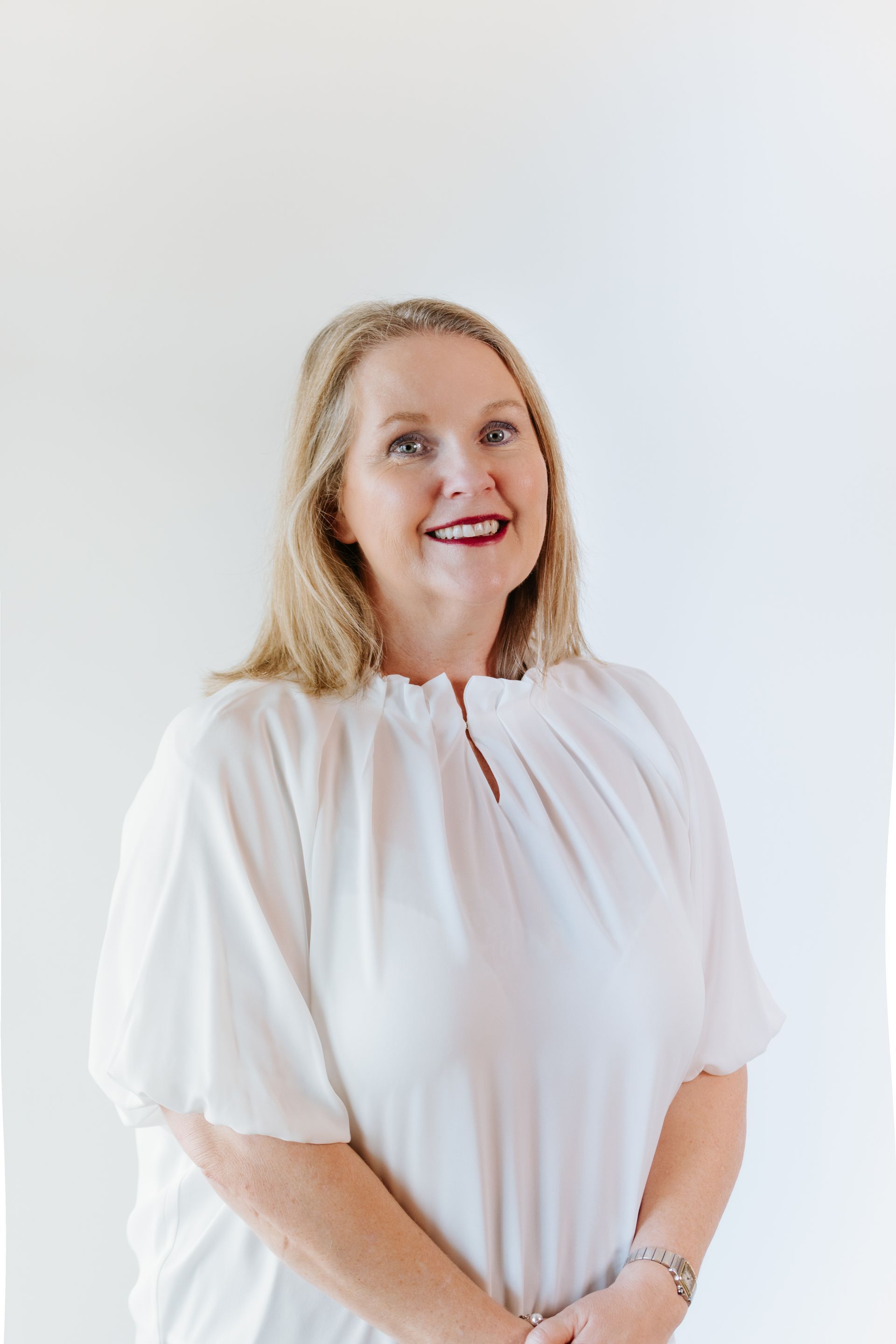 Blonde woman in a white blouse smiles at the camera against a white backdrop.