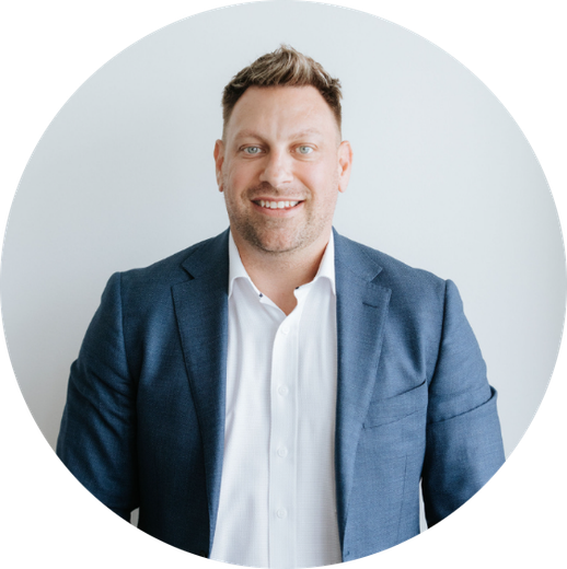 Man in blue blazer and white shirt smiles against a white backdrop.
